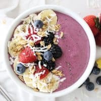 berry smoothie bowl on a white countertop topped with fresh fruit and coconut