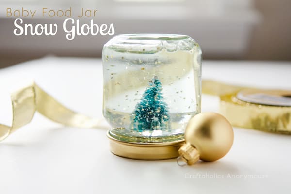 Snow globe from a baby food jar with a gold ornament next to it.