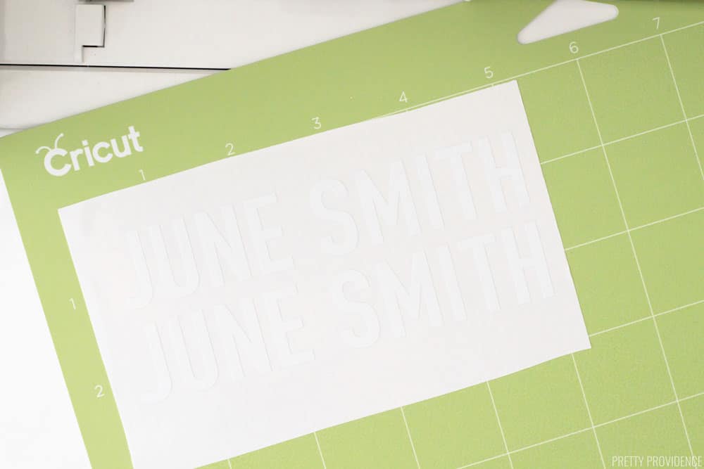 Cricut green StandardGrip cutting mat with a white rectangle of vinyl on it, two labels reading 'June Smith.'