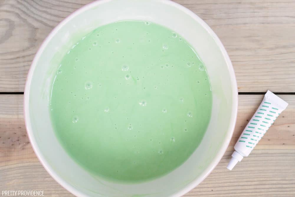 Mixing bowl holding green cake batter, a small tube of green food coloring next to it.