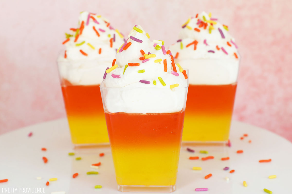 Three candy corn jello cups in a row. Yellow jello, orange jello and cool whip topped with sprinkles.