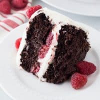 Chocolate Raspberry Cake with cream cheese frosting and raspberries inside the middle layer and on the top, as garnish on a white plate.