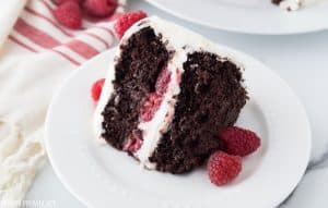 Chocolate Raspberry Cake with cream cheese frosting and raspberries inside the middle layer and on the top, as garnish on a white plate.