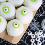 Eyeball cake balls - white cake balls with lime green frosting and candy eyeballs on a bamboo serving board and black spiderweb tea towel.