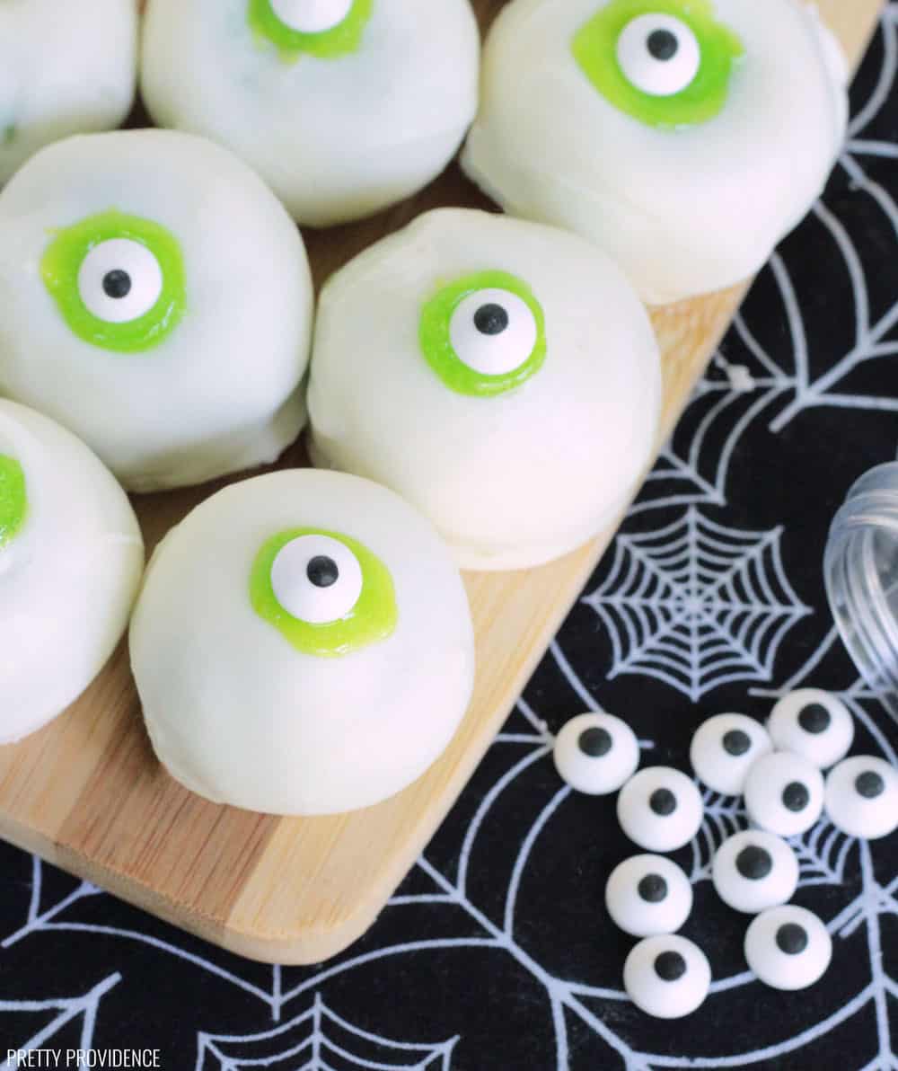 Eyeball cake balls - white cake balls with lime green frosting and candy eyeballs on a bamboo serving board and black spiderweb tea towel.