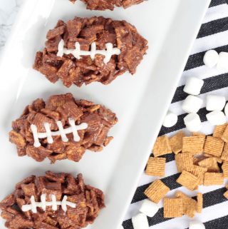 Three fotball-shaped desserts on a white plate. Golden grahams, chocolate s'mores treats with white icing for laces.