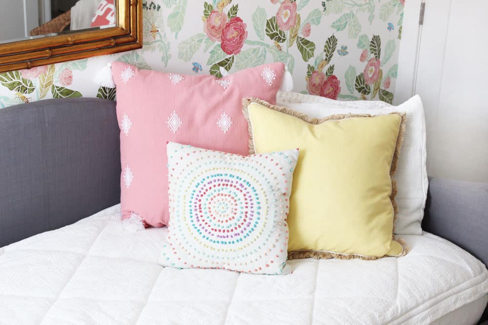 fun pink and yellow pillows on white zipper bedding against a floral wall