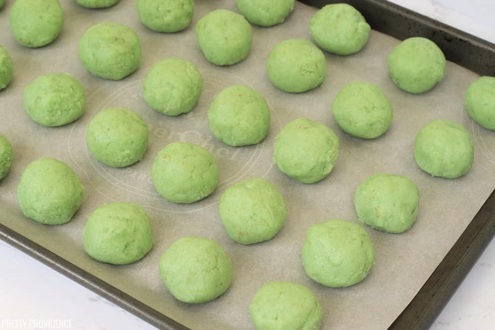 Green cake balls on parchment paper and a cookie sheet.