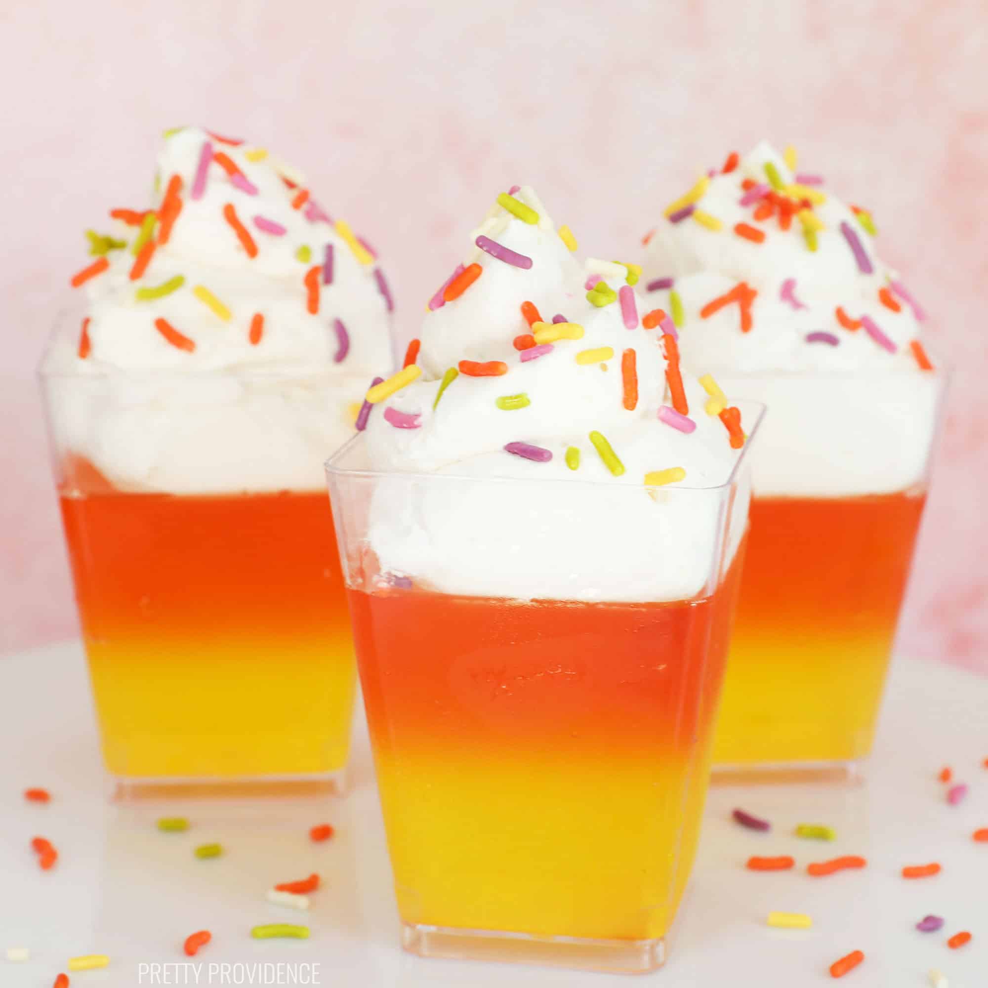 Three candy corn Jello cups, with three layers: yellow, orange, and white with sprinkles on top.