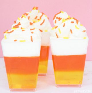 Candy Corn Jello in a clear dessert cup, yellow layer, orange layer, whipped cream and sprinkles.