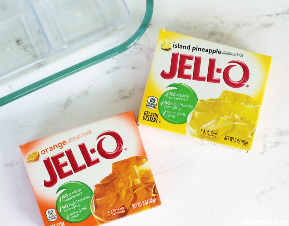 Orange Jello and Pineapple Jello boxes on a marble board, with clear dessert cups next to them.