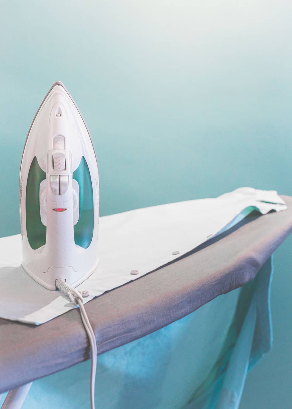 an iron ironing a white shirt against a blue wall