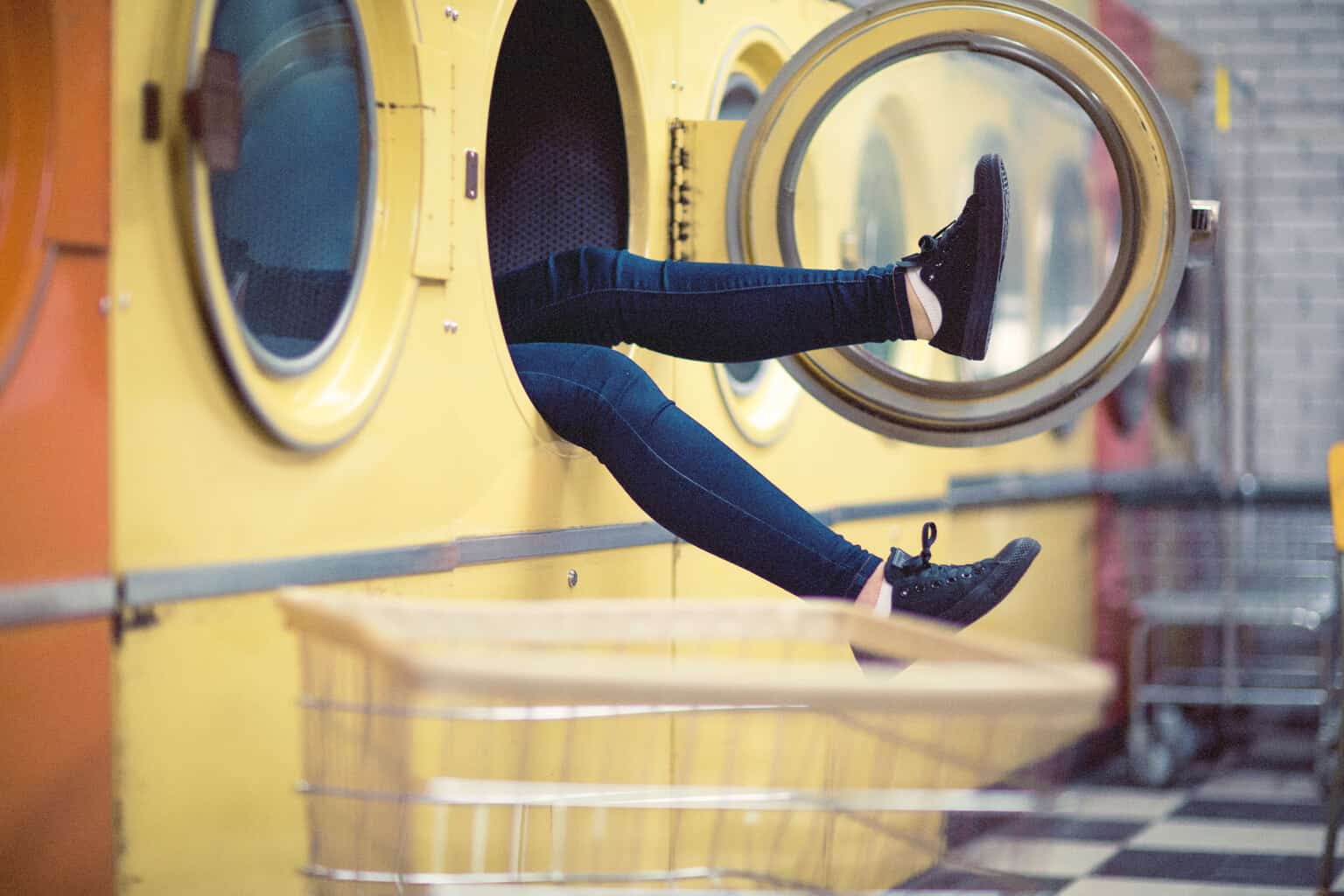 a girl in dark jeans sticking her legs out of a washing machine