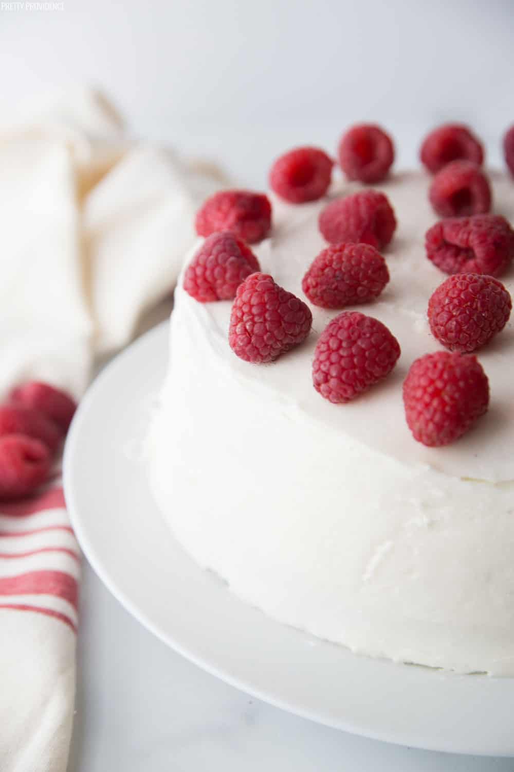 Chocolate Raspberry Cake covered in cream cheese frosting garnished with fresh raspberries on the top.