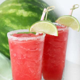 two glasses of watermelon slush with lime slices and sugar on the rims