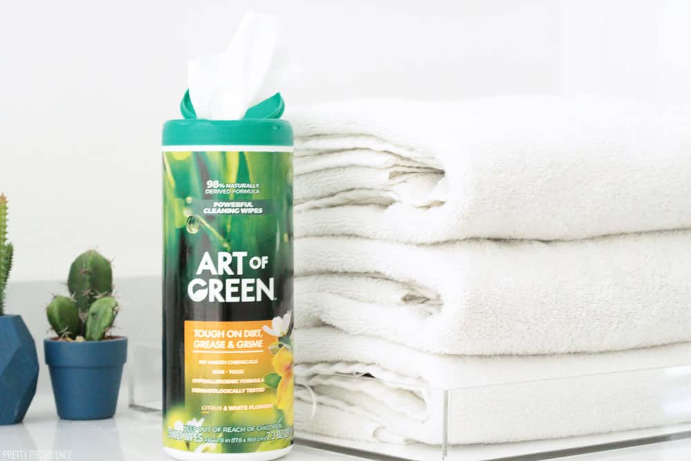 Art of Green cleaning wipes on a marble countertop with three clean white towels folded.