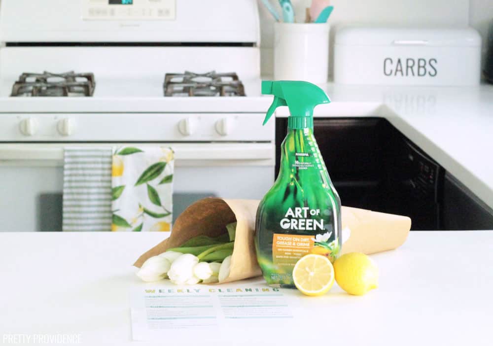 Fresh flowers, all-purpose cleaner (Art of Green) and fresh lemons on a white kitchen counter.