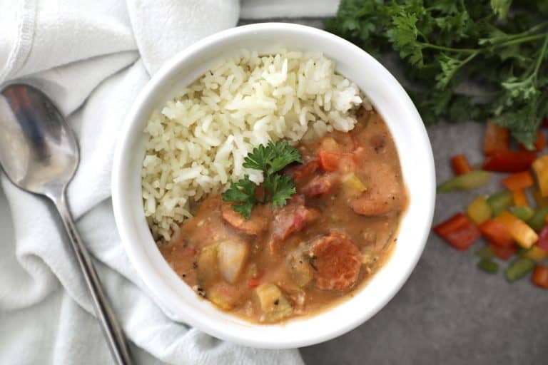 white bowl filled with gumbo and rice next to a tea towel and parsley