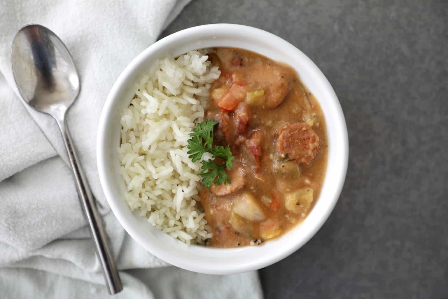 gumbo and rice garnished with fresh parsley on a concrete counter with a spoon