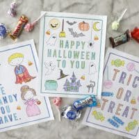 three halloween coloring pages colored in on a marble counter surrounded by candy groupings