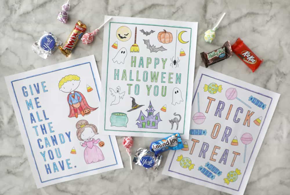 three halloween coloring pages colored in on a marble counter surrounded by candy groupings