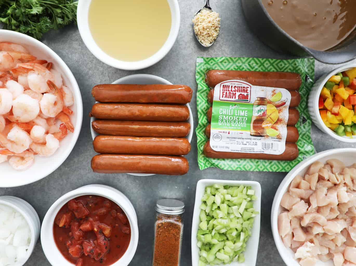 sausage, shrimp, raw chicken, veggies, chicken broth, garlic and cajun seasoning on a concrete counter
