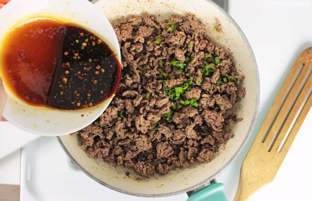 Korean beef sauce being poured over browned ground beef into a non-stick pan.
