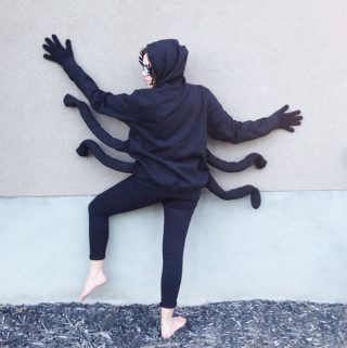 an adult woman in a spider costume against the side of a house