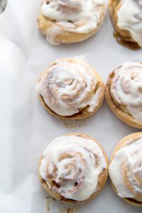 freshly frosted cinnamon rolls on a wax paper covered cookie sheet