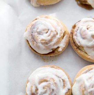 freshly frosted cinnamon rolls on a wax paper covered cookie sheet