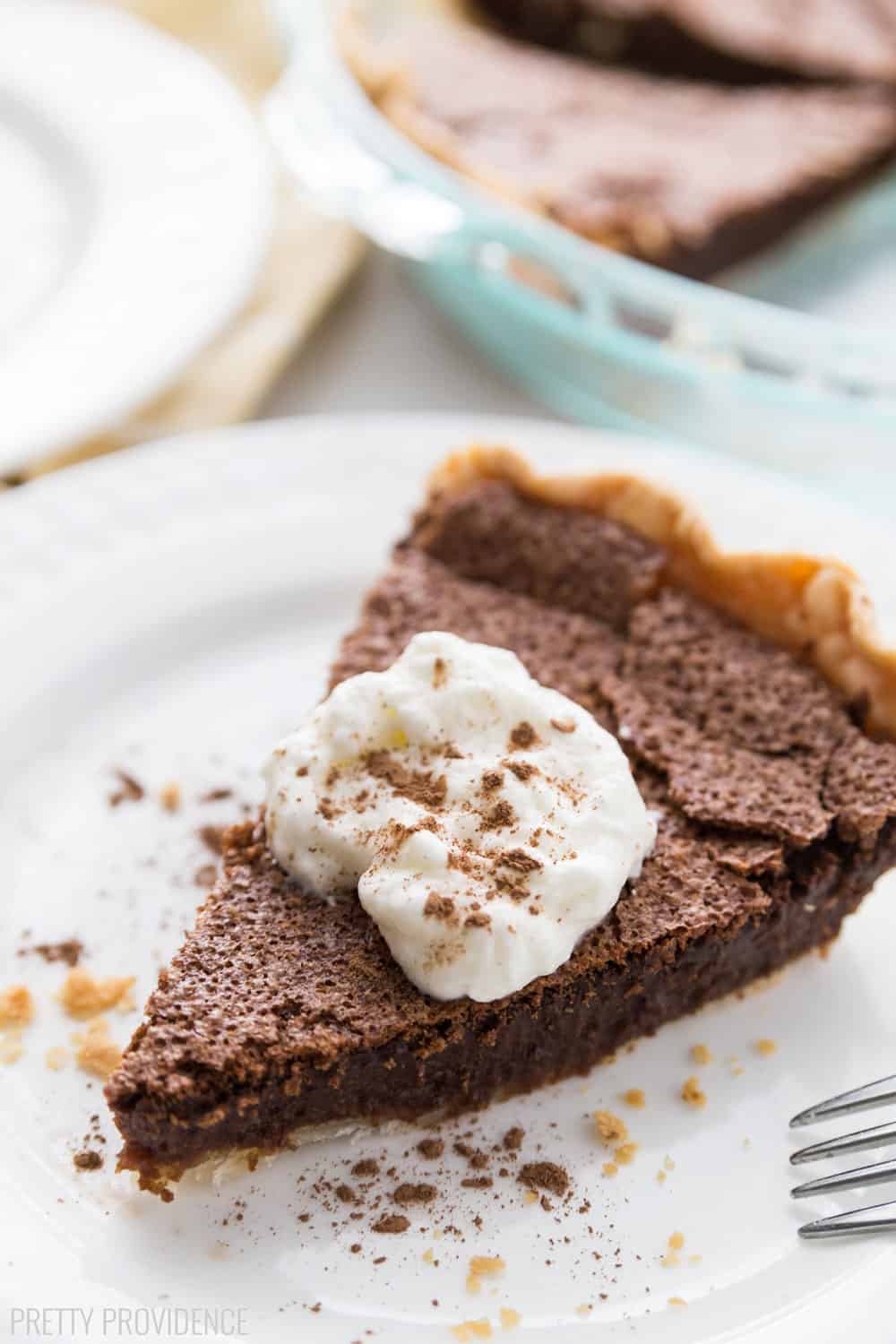 Slice of Chocolate Chess Pie topped with whipped cream on a white plate.