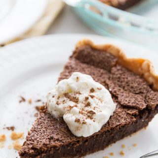 Slice of Chocolate Chess Pie on a white plate, topped with whipped cream and dusted with cocoa powder.