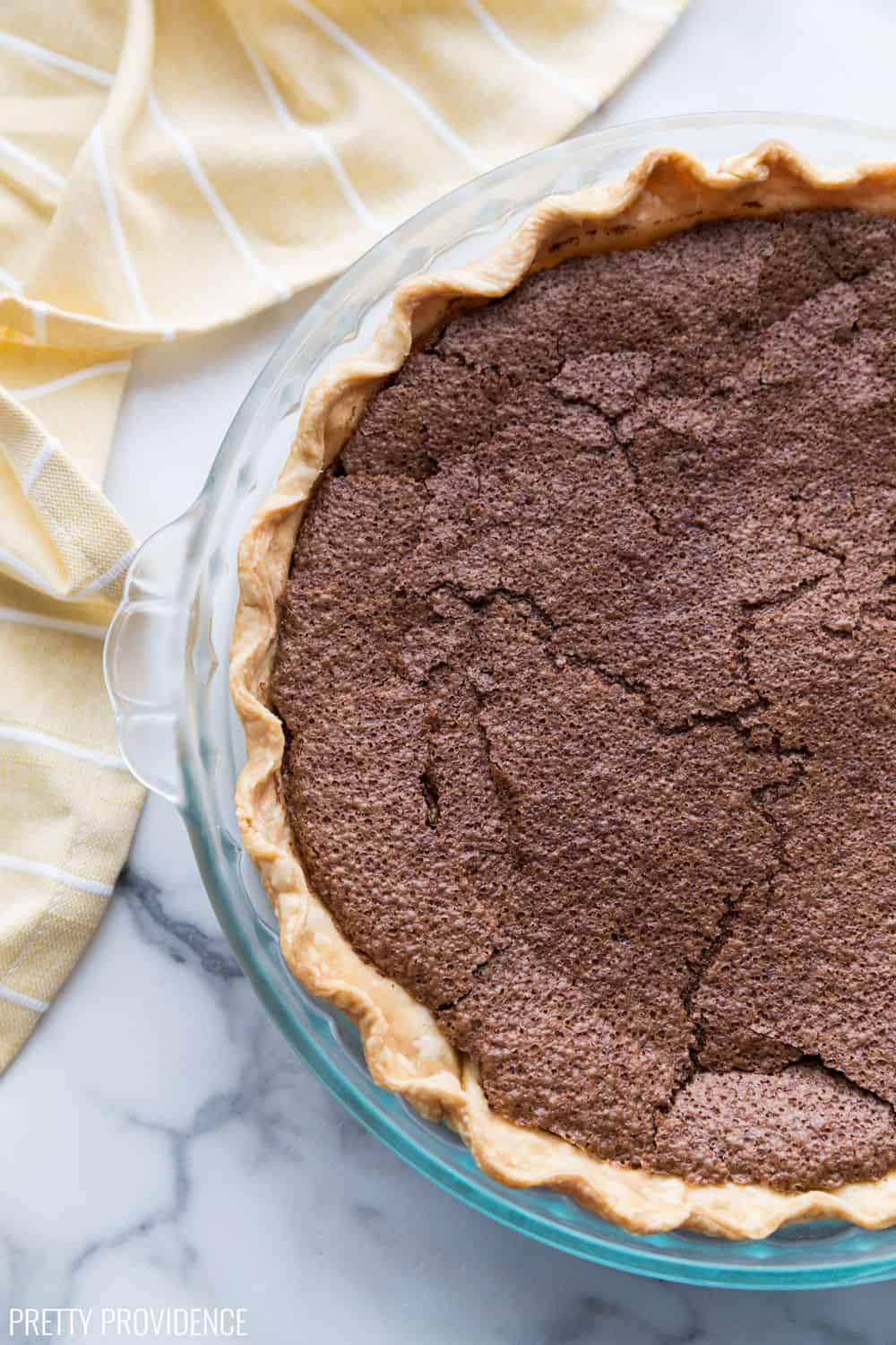 Chocolate Chess Pie, just baked in a clear pie dish on a marble surface.