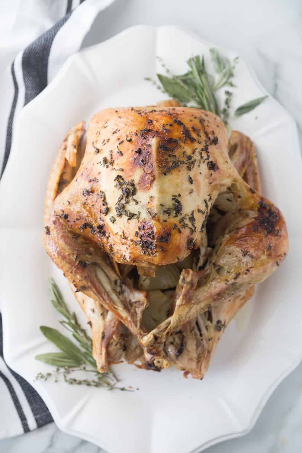 Thanksgiving Turkey on a white platter with fresh herbs sitting on a granite counter next to a tea towel