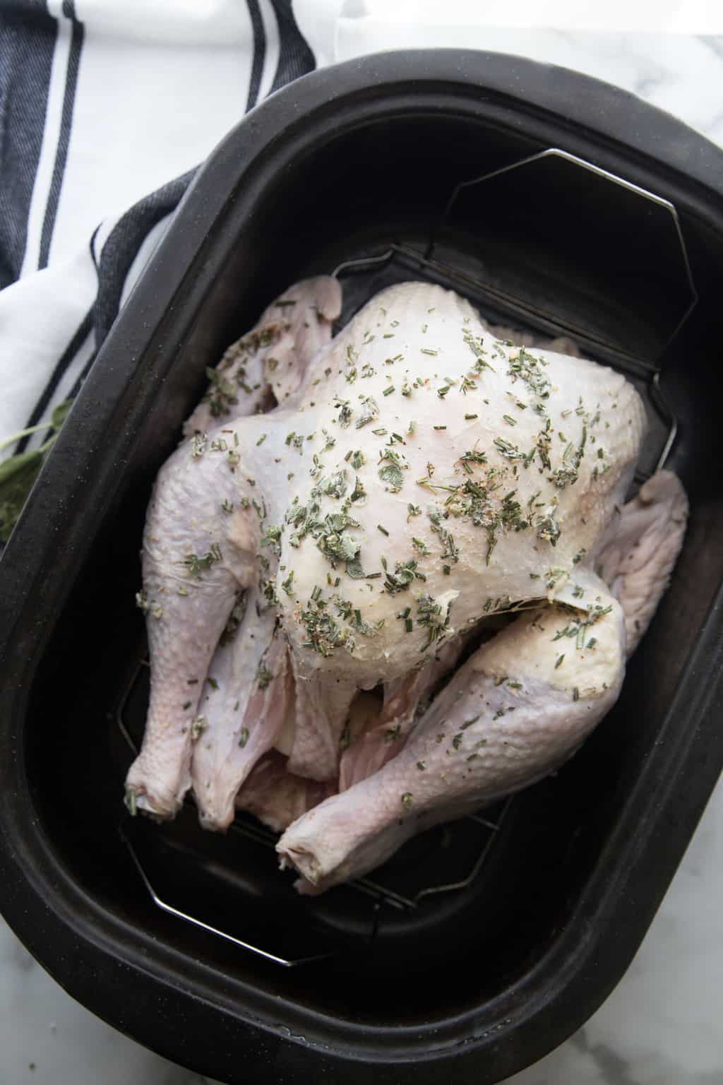 raw turkey in roasting pan covered in butter and herbs