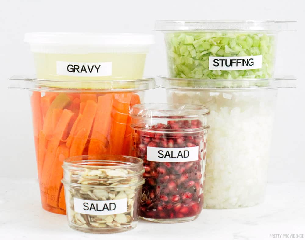 Thanksgiving prep clear containers with chopped vegetables, nuts and pomegranate seeds in them stacked on a white countertop.