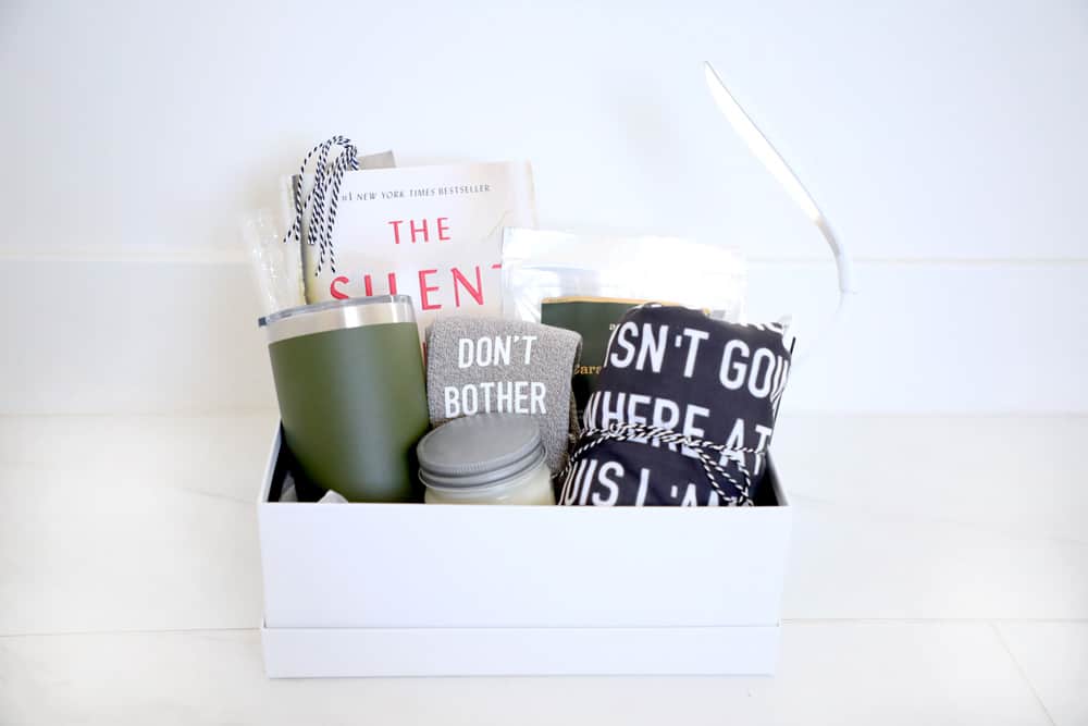 white box with a cup, book, shirt, socks, candle, book light and trail mix