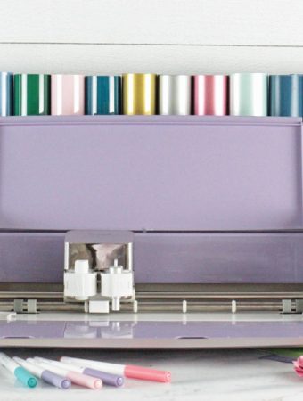 Light purple Cricut Explore Air 2 Machine with cricut accessories around it. EasyPress Mini, EasyPress 2, Cricut pens and rolls of vinyl.