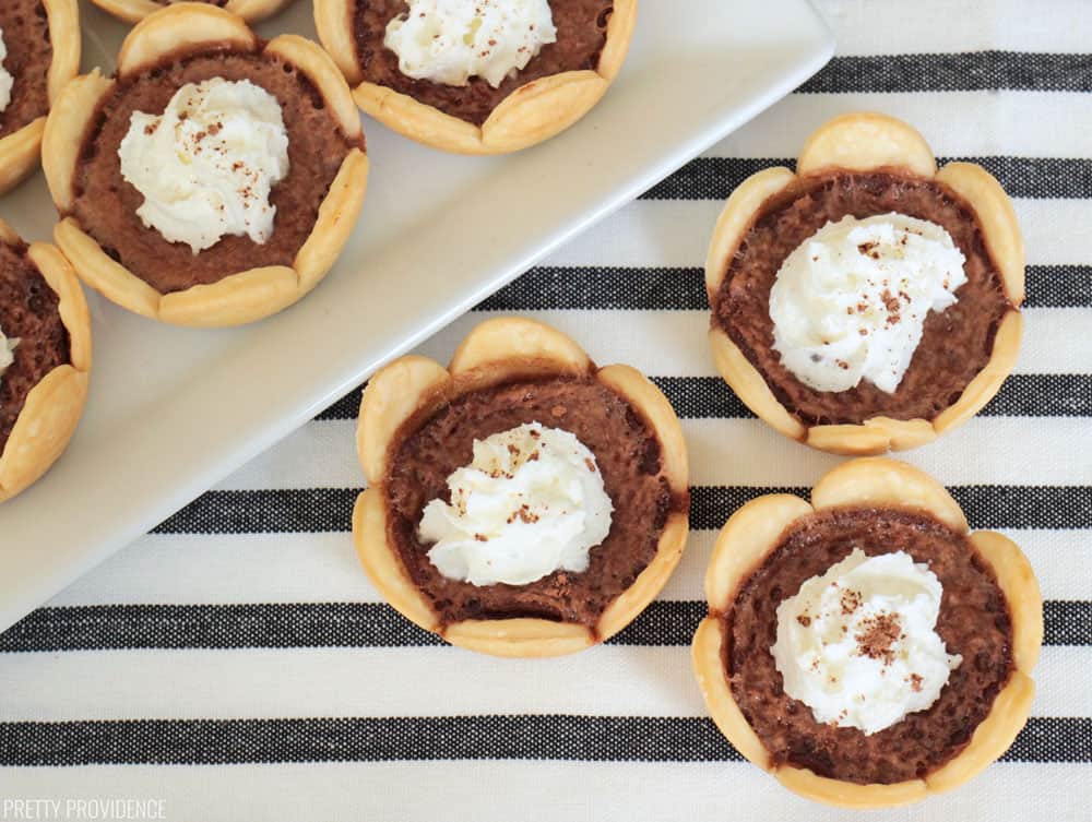 Mini Pies - Chocolate Chess mini pies with scalloped crusts and whipped cream, cocoa powder dusted on top of each.