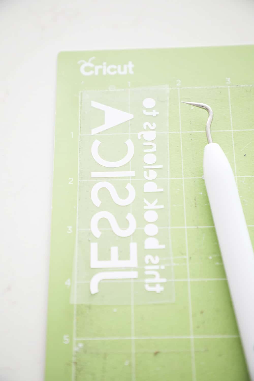 iron on text on a green cricut mat next to a weeding tool