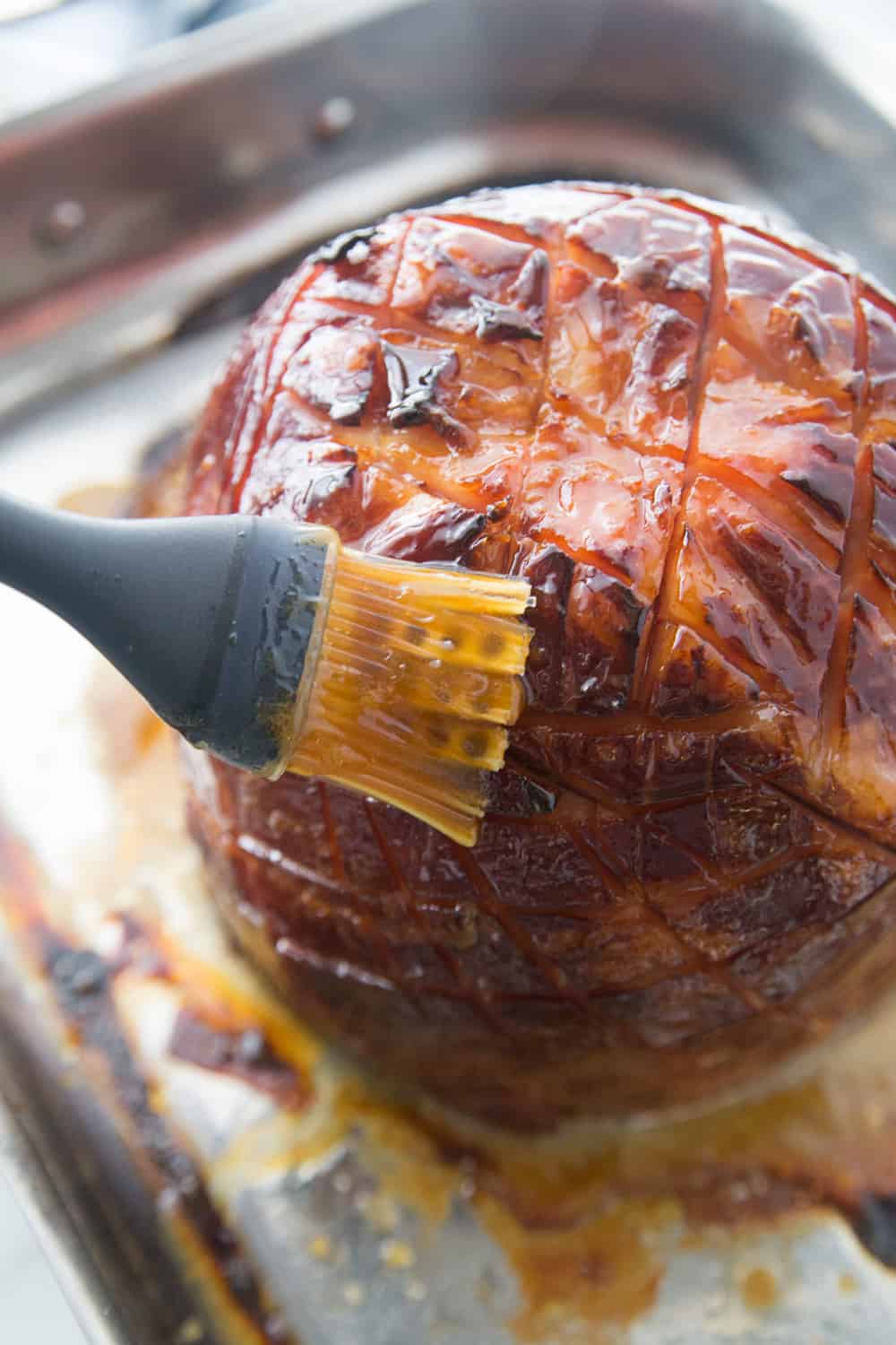 a pastry brush putting glaze on a oven baked ham on a cookie sheet