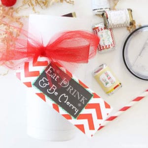 Christmas mini candy bars with a white tumbler wrapped with a red ribbon and gift tag.