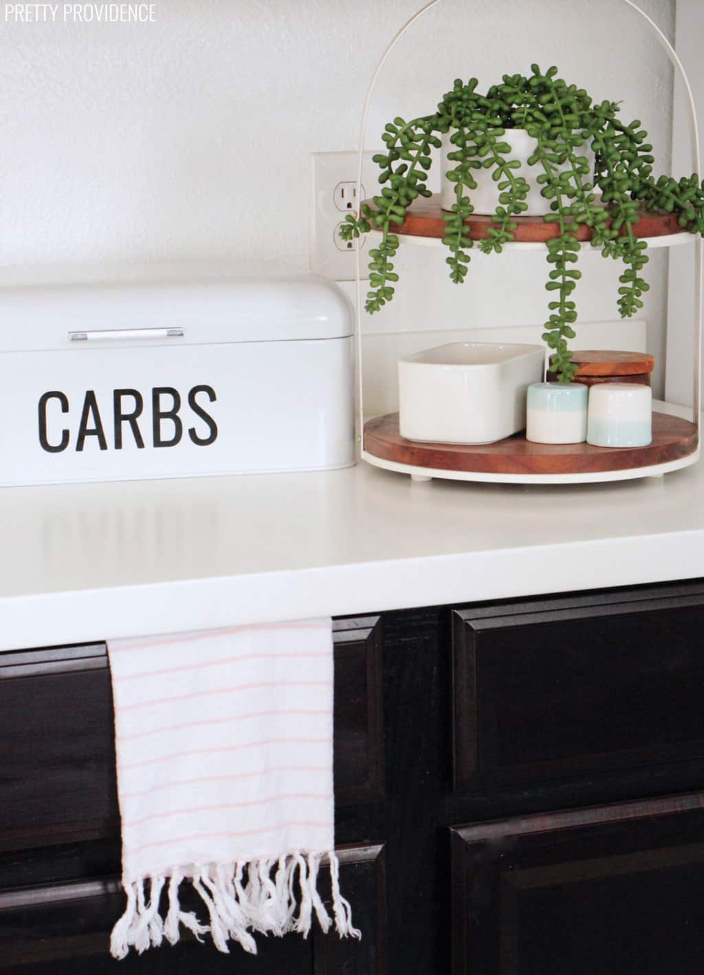 White formica countertops with espresso cabinets and a retro bread box, plant, butter dish and salt pepper shakers on it.