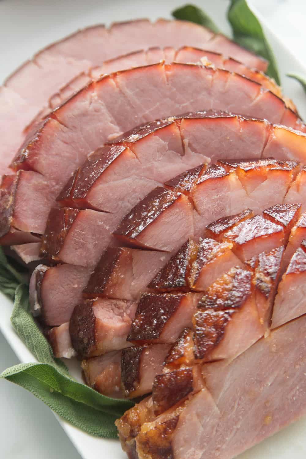 thick slices of honey baked ham on a white platter with green accents