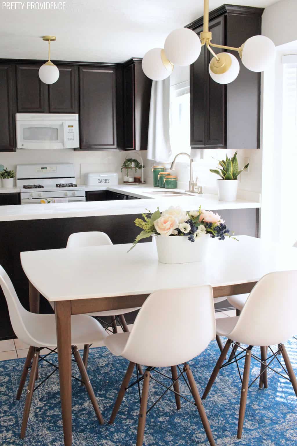 Hunter lighting Hepburn chandelier and pendant in a kitchen with mid century modern kitchen table espresso legs white table top with eames style chairs and flowers on the table.