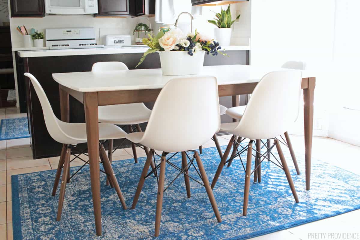 Mid century modern table and eames style chairs in a kitchen on a blue rug.