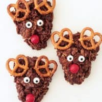 Three reindeer cookies made with cornflakes, marshmallows, pretzels, chocolate and candies.