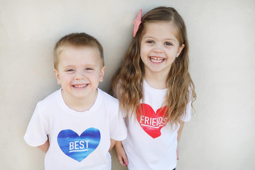 a boy who's shirt says "best" in a blue heart next to a girl who's shirt says "friends" in a pink heart