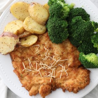 chicken schnitzel on a white plate with broccoli and potatoes