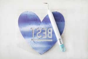 a blue, weeded, infusible ink heart that says "best" with a weeding tool over it